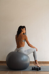 Fit woman with toned back sitting gracefully on a stability ball in yoga wear, resting after...