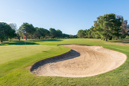 Golf course green and bunkers on a sunny day, surrounded by trees and blue sky