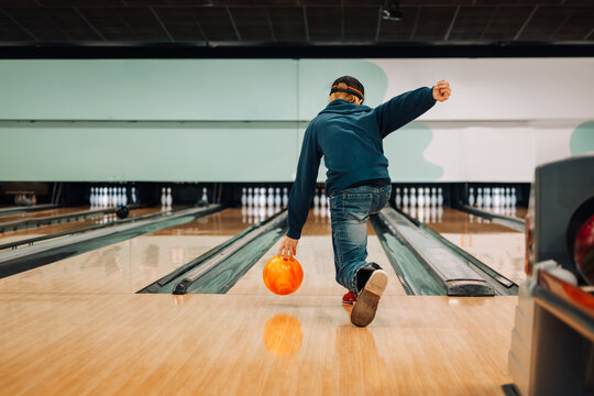 Teenage boy ten pin bowling with orange ball in brightly lit bowling alley