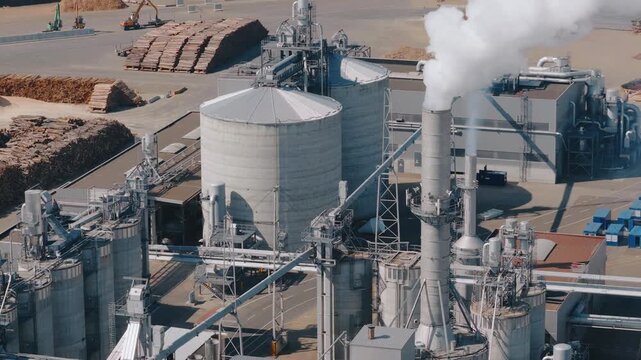 Biomass power plant emitting smoke from its chimneys near wood chips stockpile