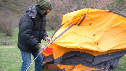 The guy inserts the arcs into the hole under them for the tent. A lone traveler sets up a tent for...