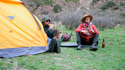 A professional guide and a tourist arranged a lunch at the campsite. Two men are sitting near a...