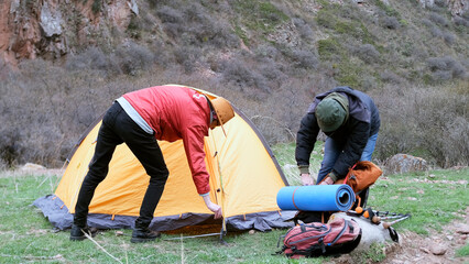 Two men set up a tent on a green lawn in the mountains. A summer hike. Tourists travel...