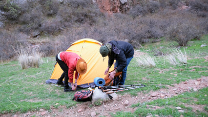 A team of two men sets up a tent on the grass near a mountain gorge. The guys are traveling together