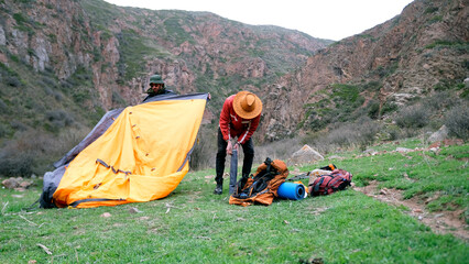 A young tourist puts metal arcs from the tent into a cover. And his partner is folding the canvas...