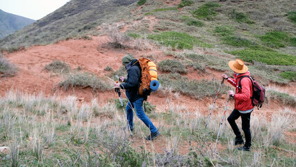 A hiking instructor and his assistant explore a new area for group hiking tours. Two people are walking along a dirt path in the mountains