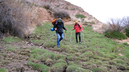 Tourists descend from the pass after a hard climb. Two friends are hiking with backpacks and trekking poles. The guide and his assistant