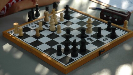 A child's hand moves a chess piece in a chess tournament. Several chess tables are lined up, a children's tournament. Chess pieces on a chess board.
