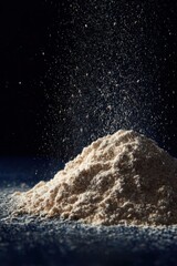 Fine flour dust rises above a mound of flour against a dark backdrop, showcasing texture and movement in cooking scene