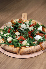 pizza artesanal recién sacada del horno con todos sus ingredientes, tomate, queso mozarela, queso, rúcula