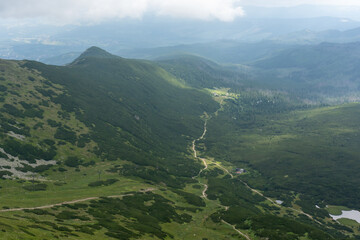 Sweeping mountain vista showing winding hiking trails through green rolling hills and forested...