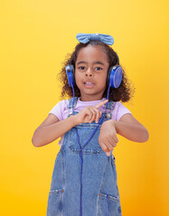 Cheerful, smiling Hispanic school-age girl with hearing aids making hand gestures,  on a yellow background.