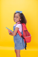 Smiling Hispanic girl of school age  with notebooks in her  hands against a yellow background.