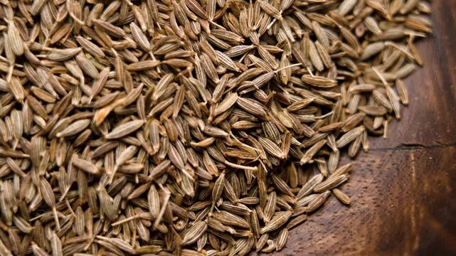 Dried cumin seeds on brown wooden texture. Aromatic spice. Organic ingredient. Top view. Macro shot. Rotation