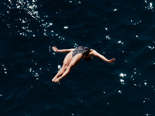 a professional female diver is jumping off a cliff into the sea