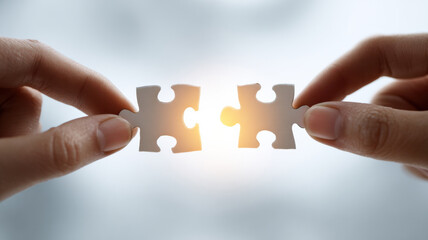 Hands fitting puzzle pieces together, symbolizing connection and solutions. The background is a soft, inviting blur that accentuates the detail of the puzzle pieces