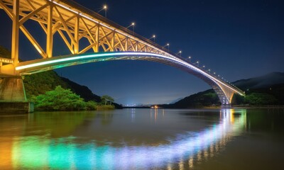 Obraz premium Illuminated bridge arching over a still river at night