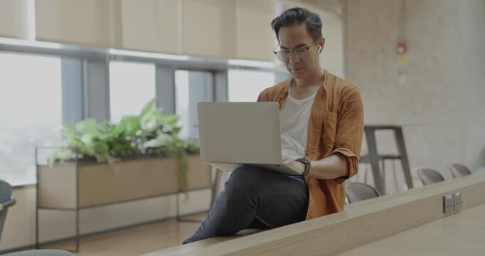 Senior Asian businessman wearing headset celebrates success during online meeting in modern co-working space. Remote work and business communication concept