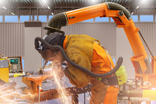 Worker in protective suit and helmet welding metal with sparks flying, using modern extraction system in industrial workshop. Welding, Metalwork, Manufacturing. - Powered by Adobe