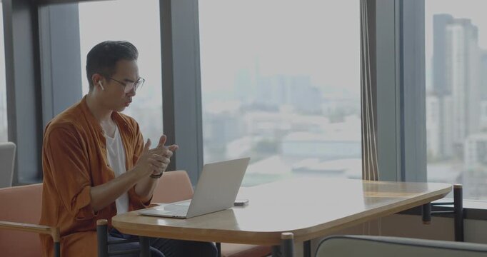 Senior Asian businessman wearing headset celebrates success during online meeting in modern co-working space. Remote work and business communication concept