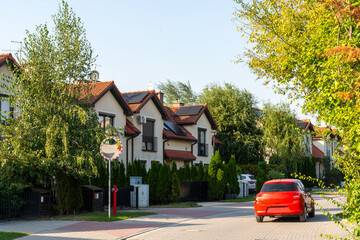 Modern suburban street with row of stylish houses with red tiled roofs, solar panels and green...