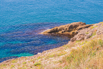 Rocky coastline in Ulcinj, Montenegro, with clear turquoise Adriatic waters gently lapping against the shore. Sunlit waves reveal underwater textures and vibrant marine hues.