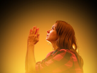 Side view of woman praying with hands together, looking upward in spiritual reflection on glowing...
