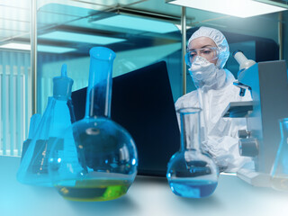 Scientist in protective suit working at laptop in high-security laboratory surrounded by glassware...