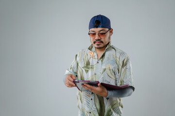 Casual man wearing a floral shirt and cap interacting with a tablet against a plain background...