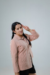 Young woman in casual outfit with long dark hair posing against a neutral background, making a...