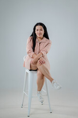 Confident woman sitting on a stool in casual outfit with long hair in a minimalistic studio...