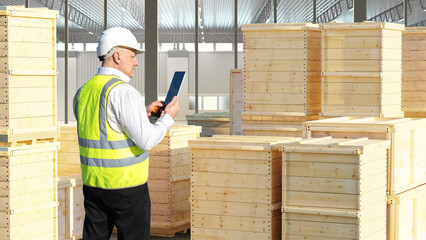 Fototapeta premium Man warehouse specialist. Worker among wooden containers. Storekeeper among transport tare. Warehouse specialist stands in yellow vest. Experienced storekeeper inside industrial building
