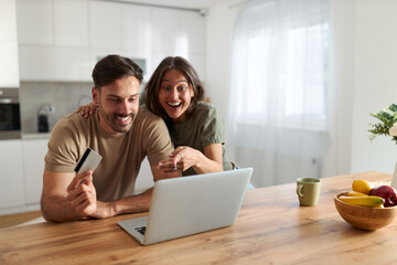 Happy couple using credit card for online shopping over laptop at home.	