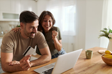 Happy couple using credit card for online shopping over laptop at home.	