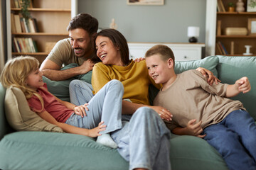 Cheerful parents and their small kids having fun while talking in the living room.