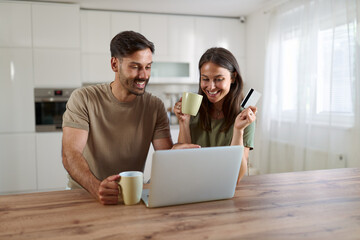 Happy couple using credit card for online shopping over laptop at home.	