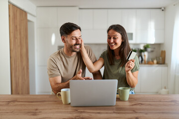 Happy couple using credit card for online shopping over laptop at home.	