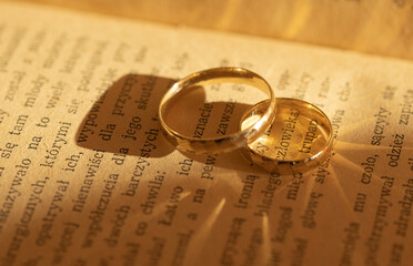 gold wedding rings create highlights and shadows on the pages of a yellowed book