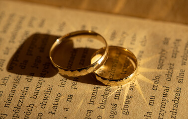 gold wedding rings with a non-uniform texture create glare on the pages of a yellowed book