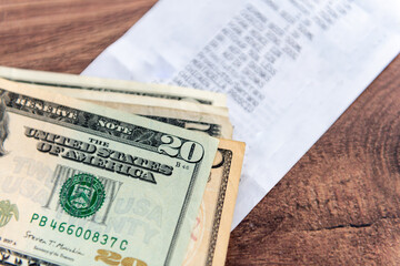 A stack of US Dollar bills on a supermarket grocery till receipt on a table. A US cost of living concept.