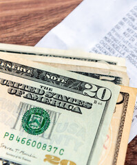 Close up of a pile of US Dollar bills and a supermarket grocery receipt on a table. A US cost of...