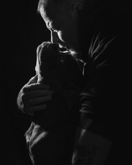 Black and white portrait of a blue Old English Bulldog sitting in arms of owner, looking up at human with deep eye contact, showing strong emotional bond, trust and affection