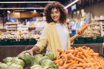 Woman choosing carrots and cabbage in supermarket