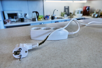 An extension tee with charred power cord lies on table, unsuitable for further use.