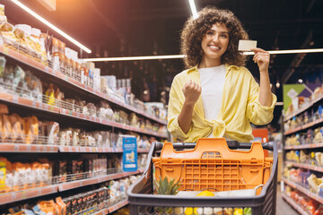 Woman Holding Loyalty Card and Pushing Shopping Cart in Supermarket