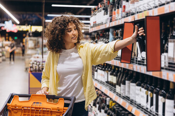 Woman choosing wine bottle from supermarket shelf