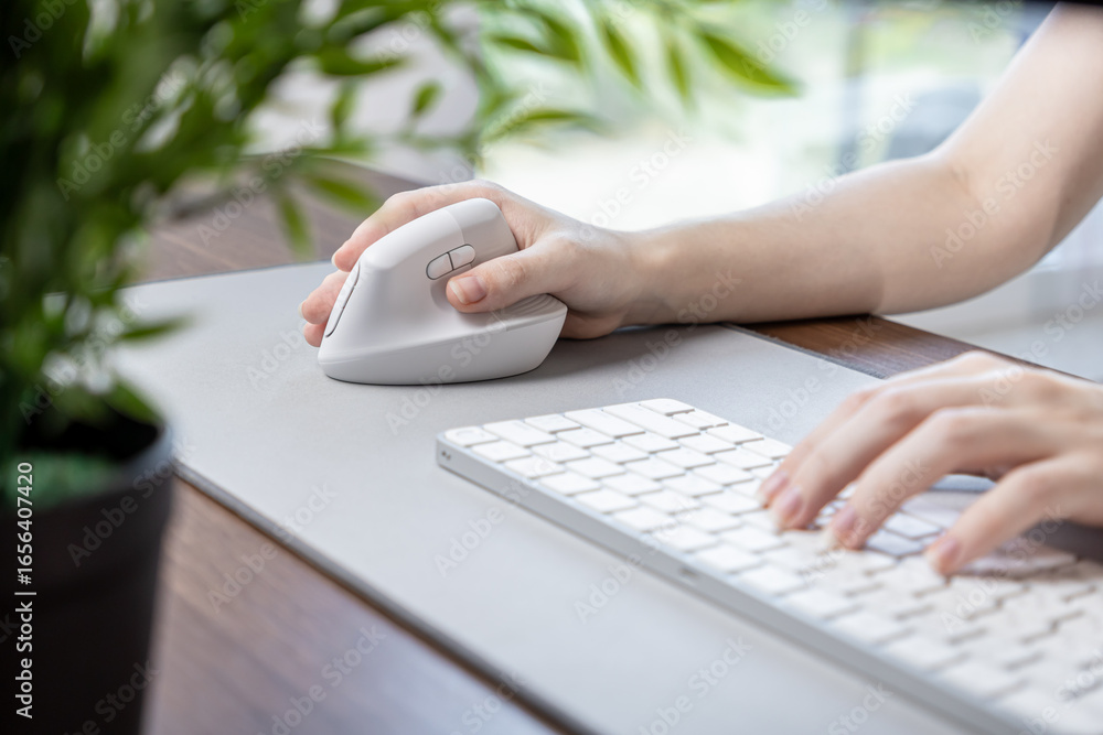 Fototapete female hand using a white vertical ergonomic mouse on a grey desk pad with a keyboard, emphasizing c