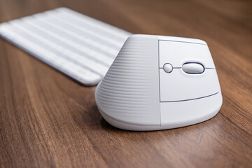 Ergonomic white vertical computer mouse on a wooden desk with a blurred keyboard, promoting wrist...
