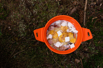 Mixing ingredients for a hearty outdoor meal in a bright orange pot in the woods. Gorgany range....
