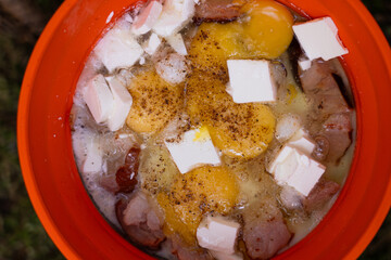 Mixing ingredients for a hearty outdoor meal in a bright orange pot in the woods. Gorgany range....
